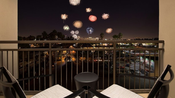 A balcony with two chairs and a small table, overlooking a cityscape with buildings and a parking area.