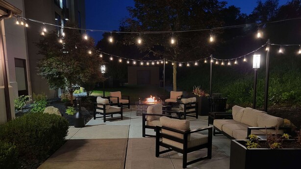 An outdoor patio area with string lights, a fire pit, and outdoor furniture.
