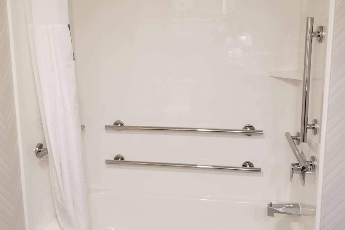 A white bathtub with a shower head, grab bars, and a handheld shower attachment.
