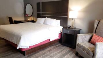 Habitación de hotel con una cama grande, una mesita de noche con lámpara, una silla y un espejo montado en la pared.