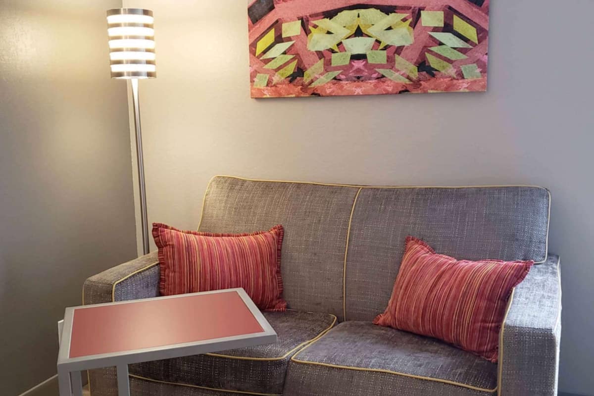 A modern living room with a grey sofa, two red pillows, a small table, and a colorful abstract painting on the wall.