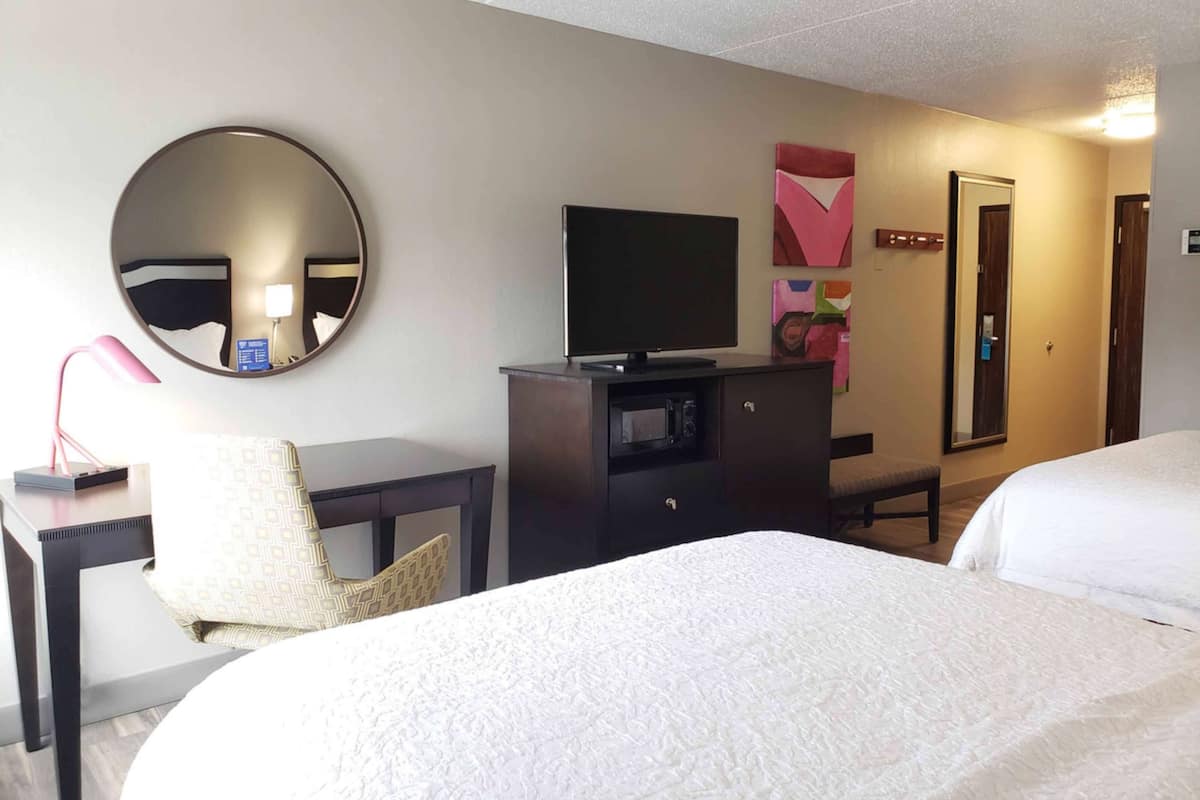 A hotel room with a bed, a desk with a computer, a chair, a television, and a mirror.