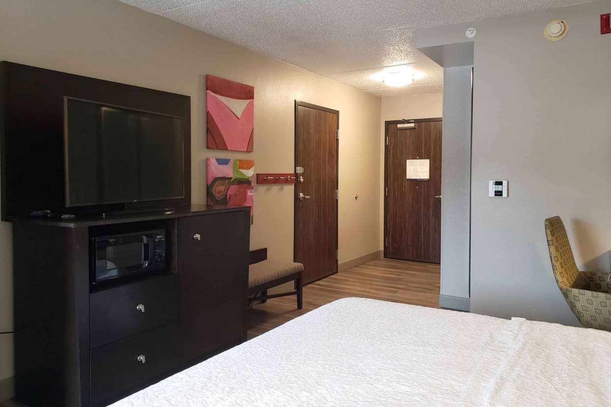 A hotel room with a bed, a TV on a dresser, a chair, and a door.
