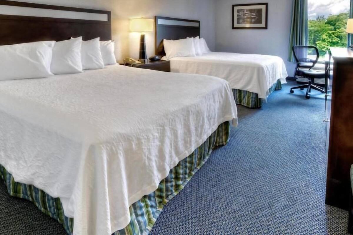 A hotel room with two beds, a desk, a chair, and a window with a view.