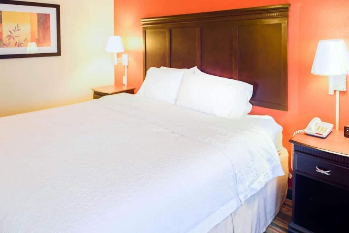 A hotel room with a large bed, two bedside lamps, a nightstand with a phone, and a framed picture on the wall.