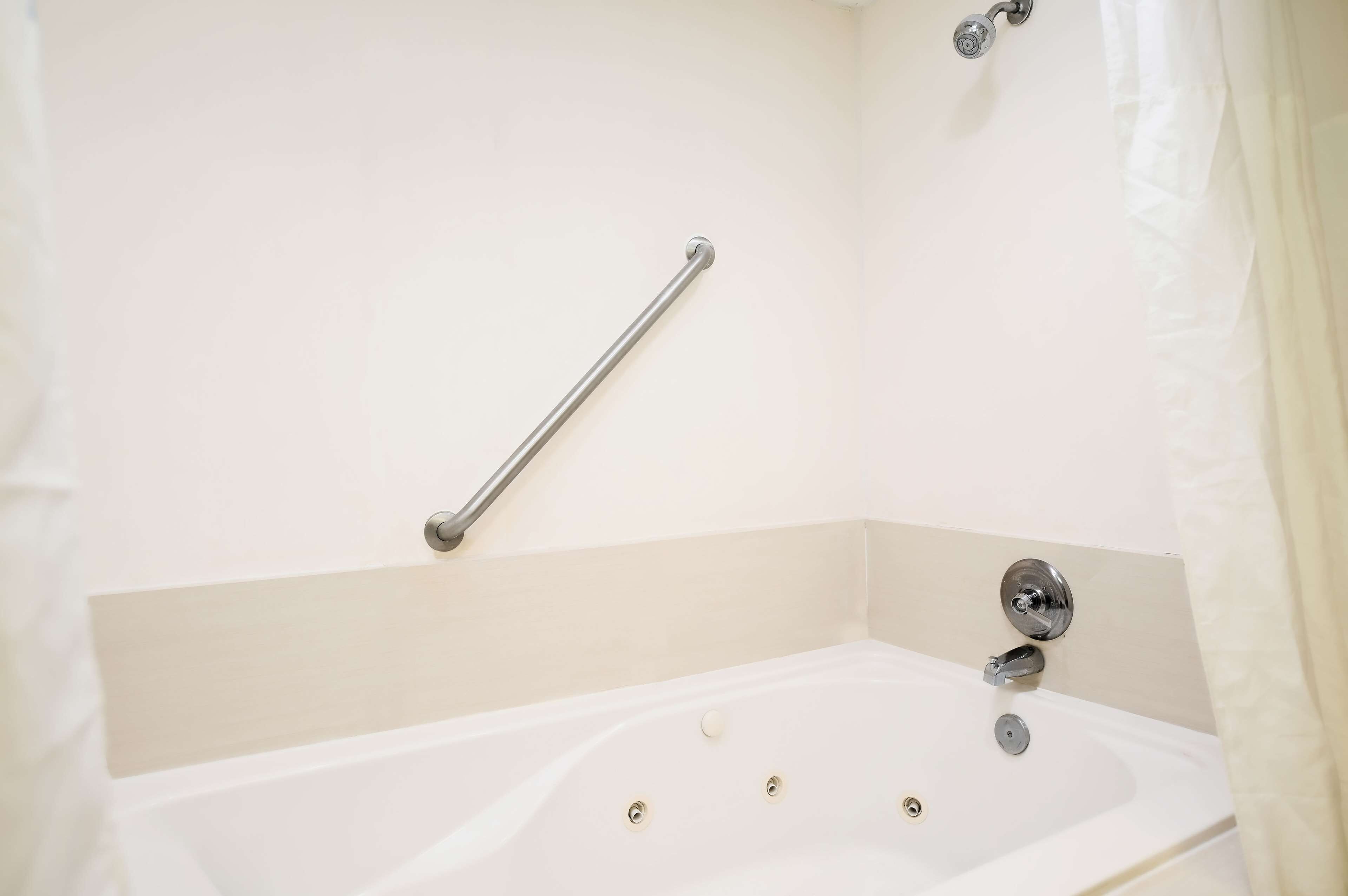 Un baño con una bañera blanca, una barra de apoyo y una cortina de ducha.