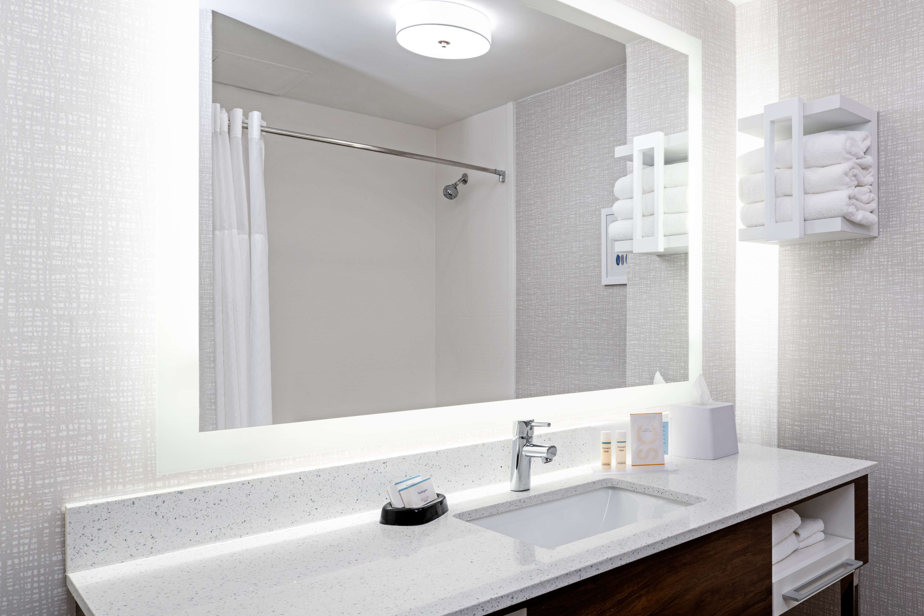 A modern bathroom with a large mirror, a sink, a towel rack, and a shower area.