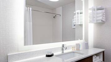 A modern bathroom with a large mirror, a sink, a towel rack, and a shower area.
