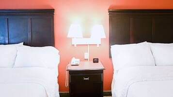 A hotel room with two beds, a nightstand with a lamp, a phone, and a clock.