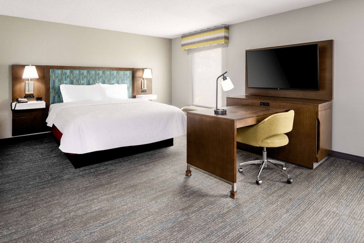 A hotel room with a bed, desk, chair, TV, and bedside lamps.