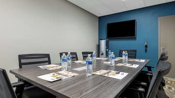 Un salón de conferencias con una larga mesa, sillas, botellas de agua y folletos informativos.