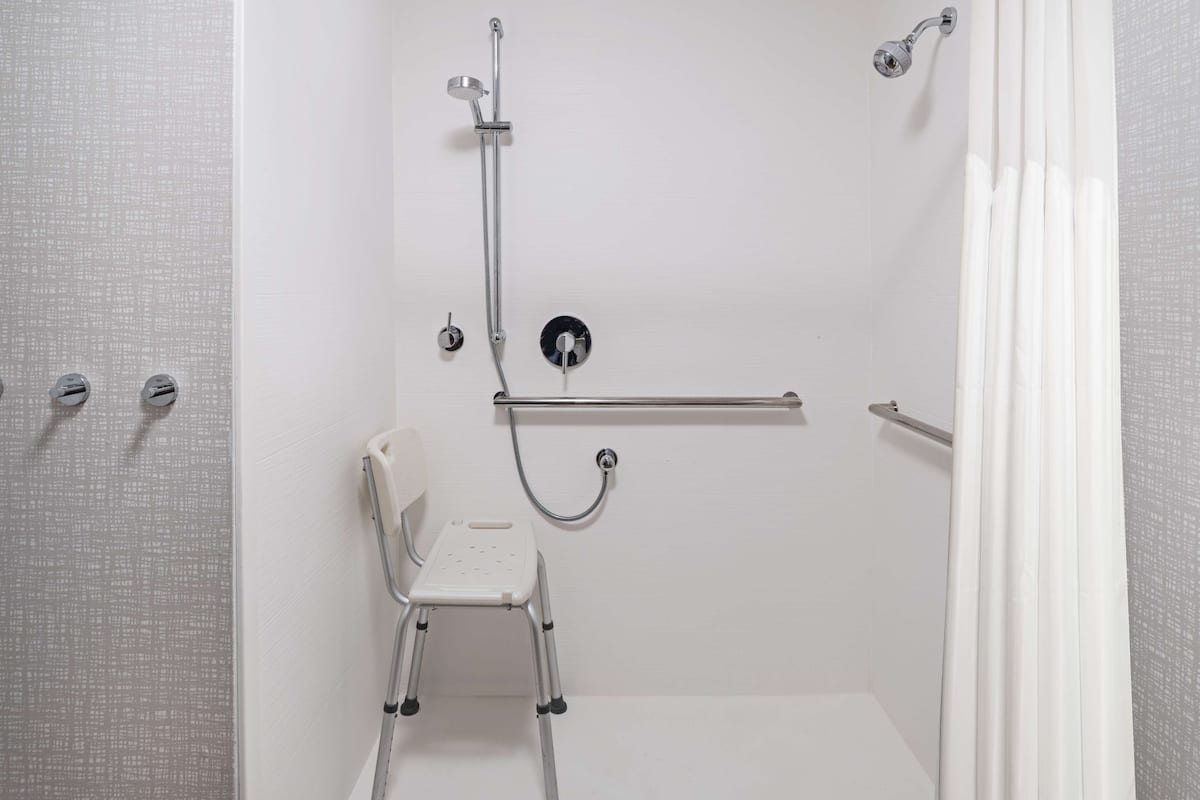 A walk-in shower with a handheld showerhead, a handheld shower seat, and a grab bar.