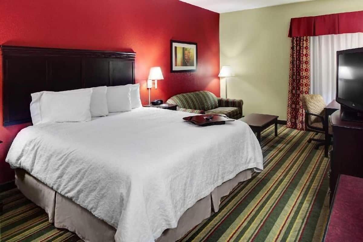 A hotel room with a large bed, two bedside tables, a television, a chair, and a window with curtains.