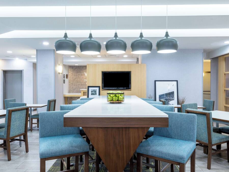 A modern dining area with a central table, blue upholstered chairs, and pendant lighting.
