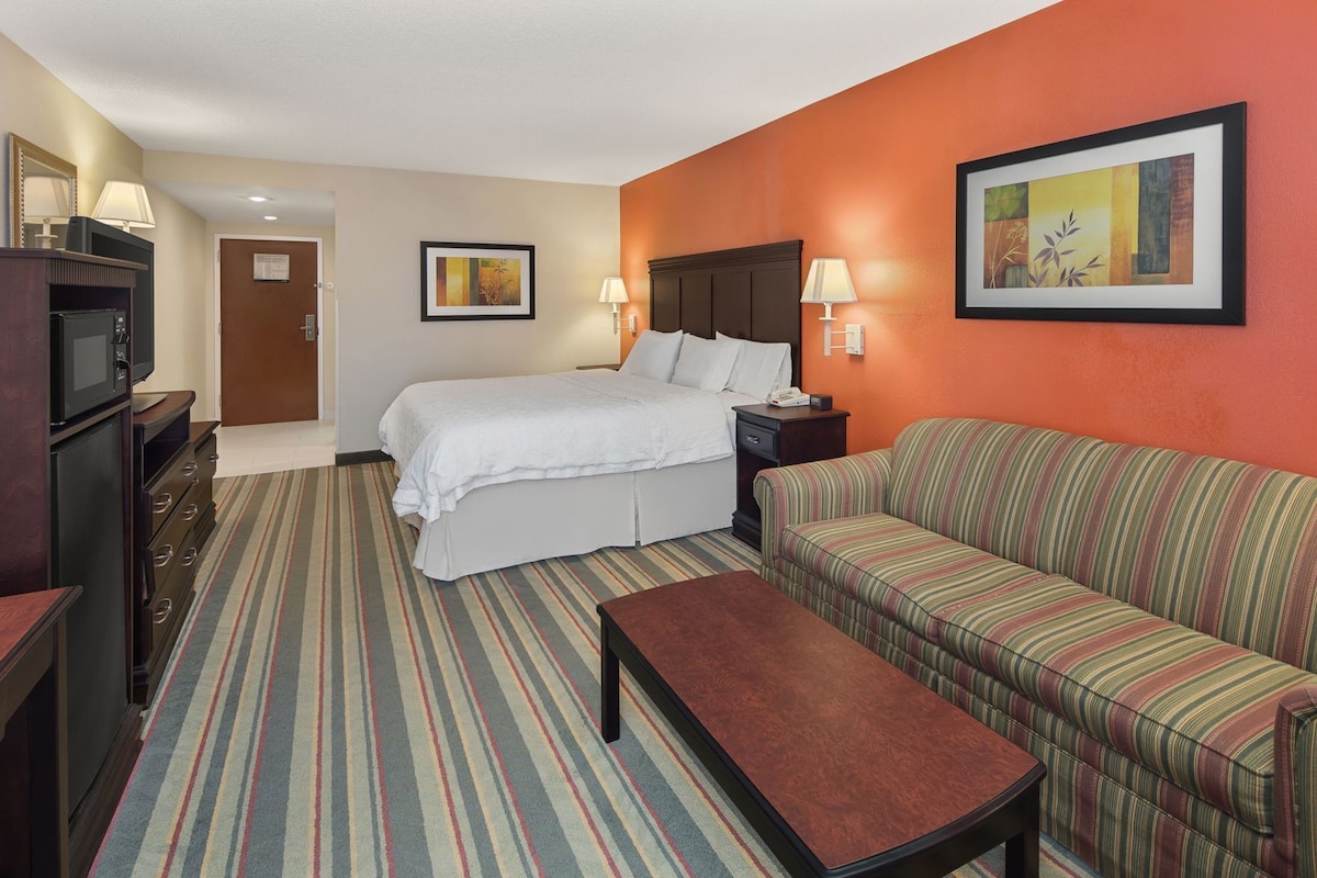 A hotel room with a bed, a sofa, a TV, a desk, and a lamp.