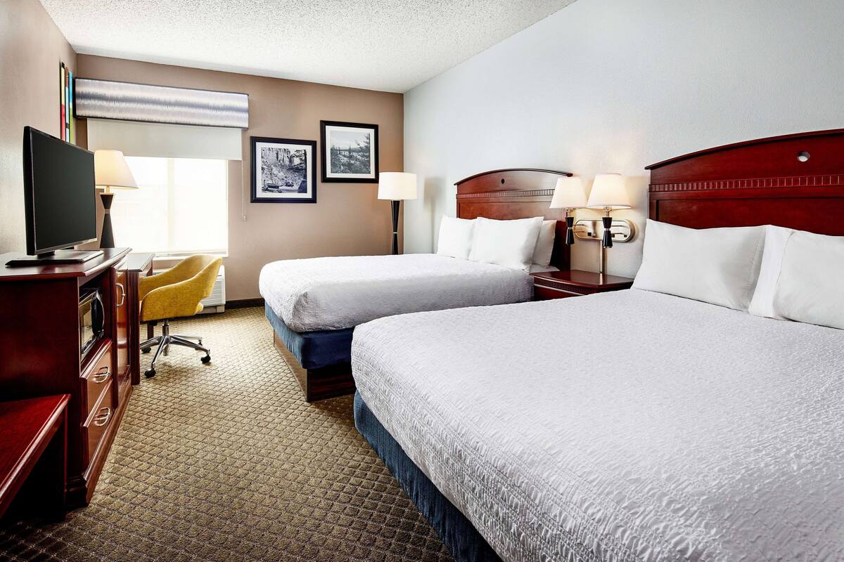 A hotel room with two beds, a desk with a computer, a chair, and a television.