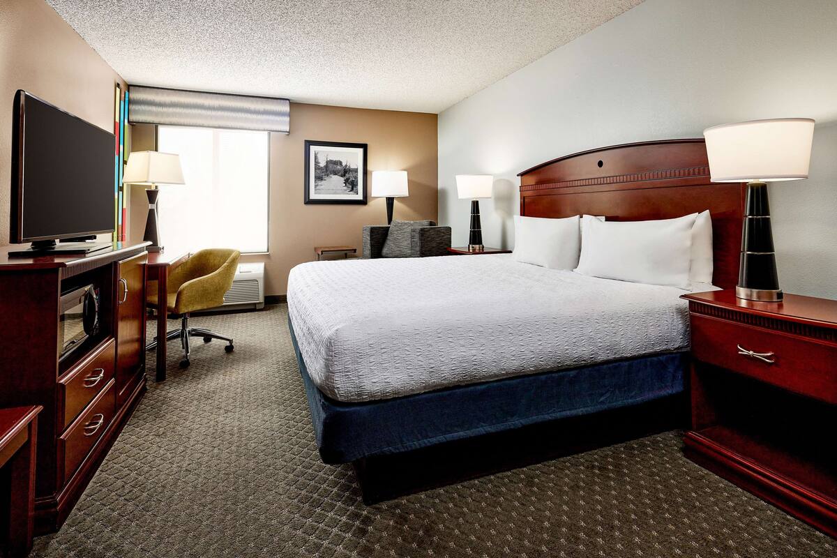 A hotel room with a large bed, a television, a desk with a computer, and a chair.