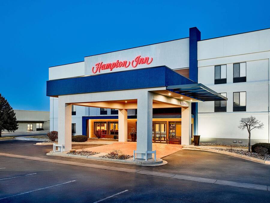 Um hotel Hampton Inn moderno com entrada destacada, área externa coberta e céu claro.