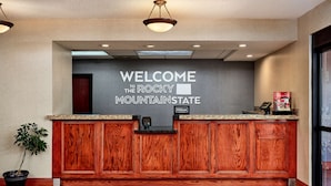 A reception desk with a "Welcome to the Rocky Mountain State" sign, a wooden panel design, and a potted plant. - Hampton Inn Longmont (Longmont)