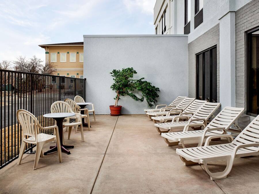 Un patio con sillones de descanso y mesas, una planta en maceta y un edificio al fondo.