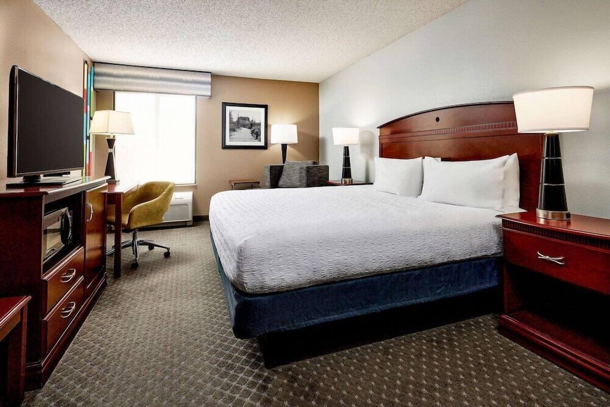 A hotel room with a large bed, a television, a desk with drawers, a chair, and two bedside lamps.