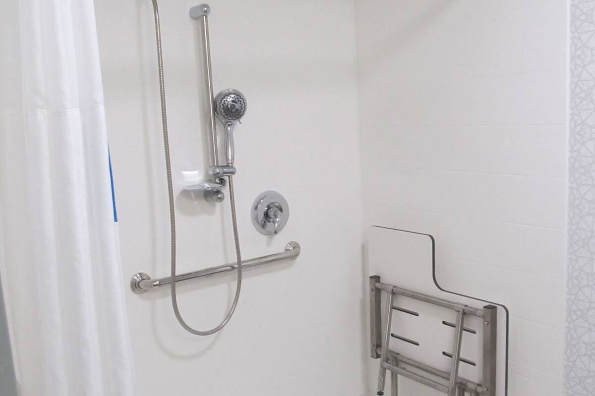A shower area with a grab bar, a handheld showerhead, and a wall-mounted control.
