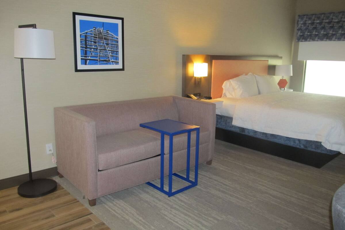 A hotel room with a bed, a sofa, a small table, a lamp, and a framed picture on the wall.