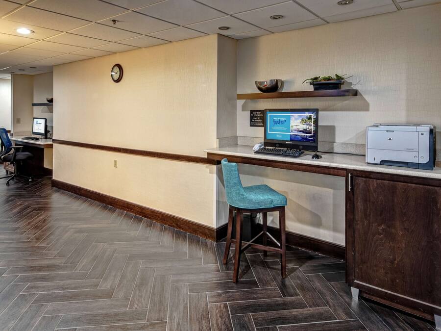 A reception area with a wooden herringbone floor, a desk with a computer and printer, a blue chair, and a clock on the wall.