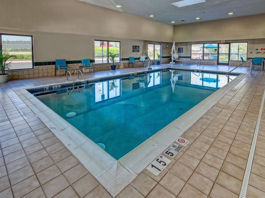 An indoor swimming pool with clear water, tiled floor, and blue chairs along the sides.