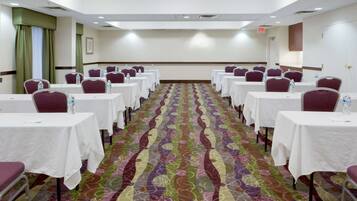 A conference room with rows of tables and chairs, a patterned carpet, and a plain wall with a framed picture.