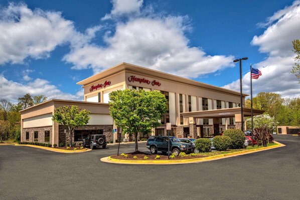 A Hampton Inn hotel with a parking lot, a flag, and a clear sky.