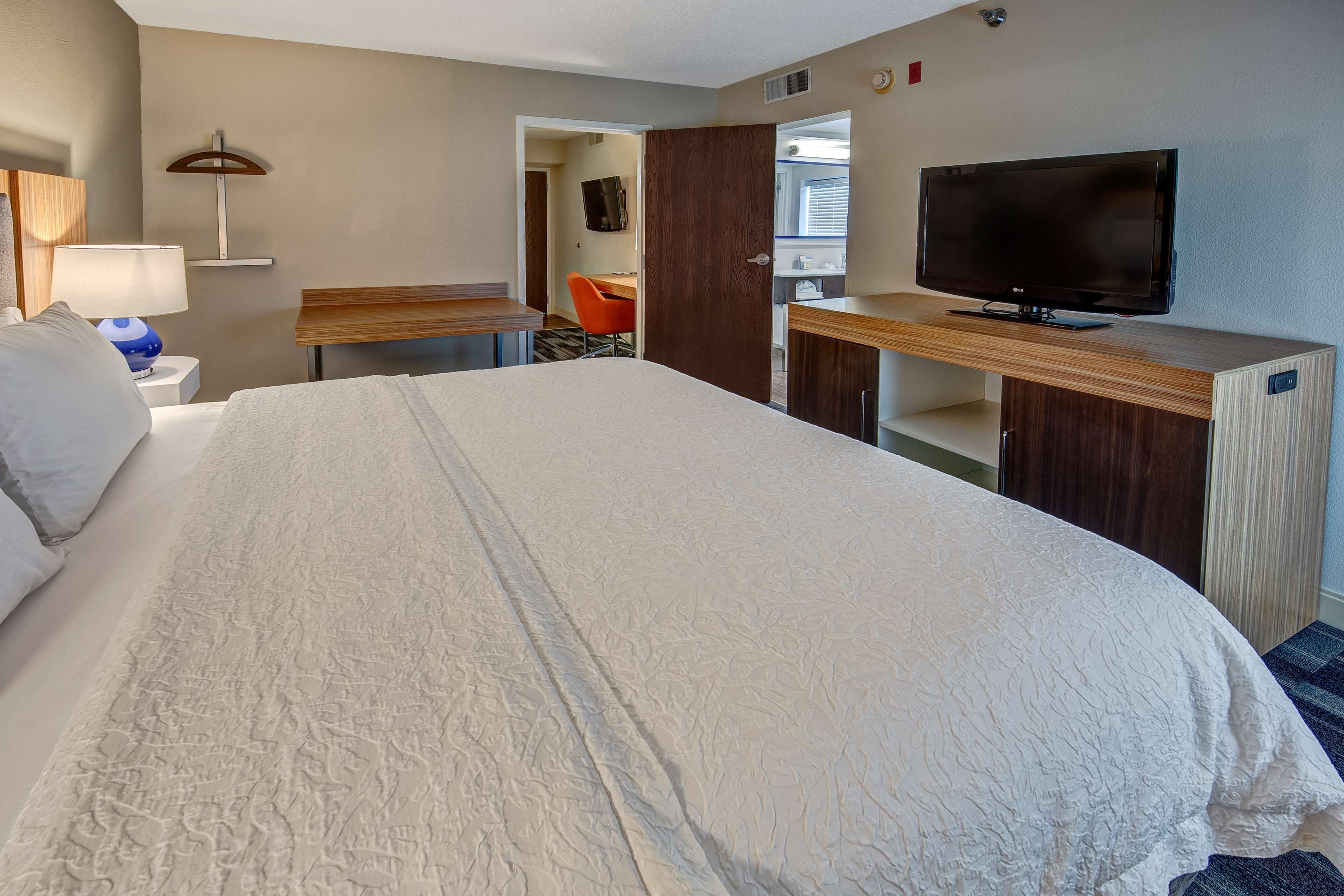A hotel room with a large bed, a desk, a television, and a chair.