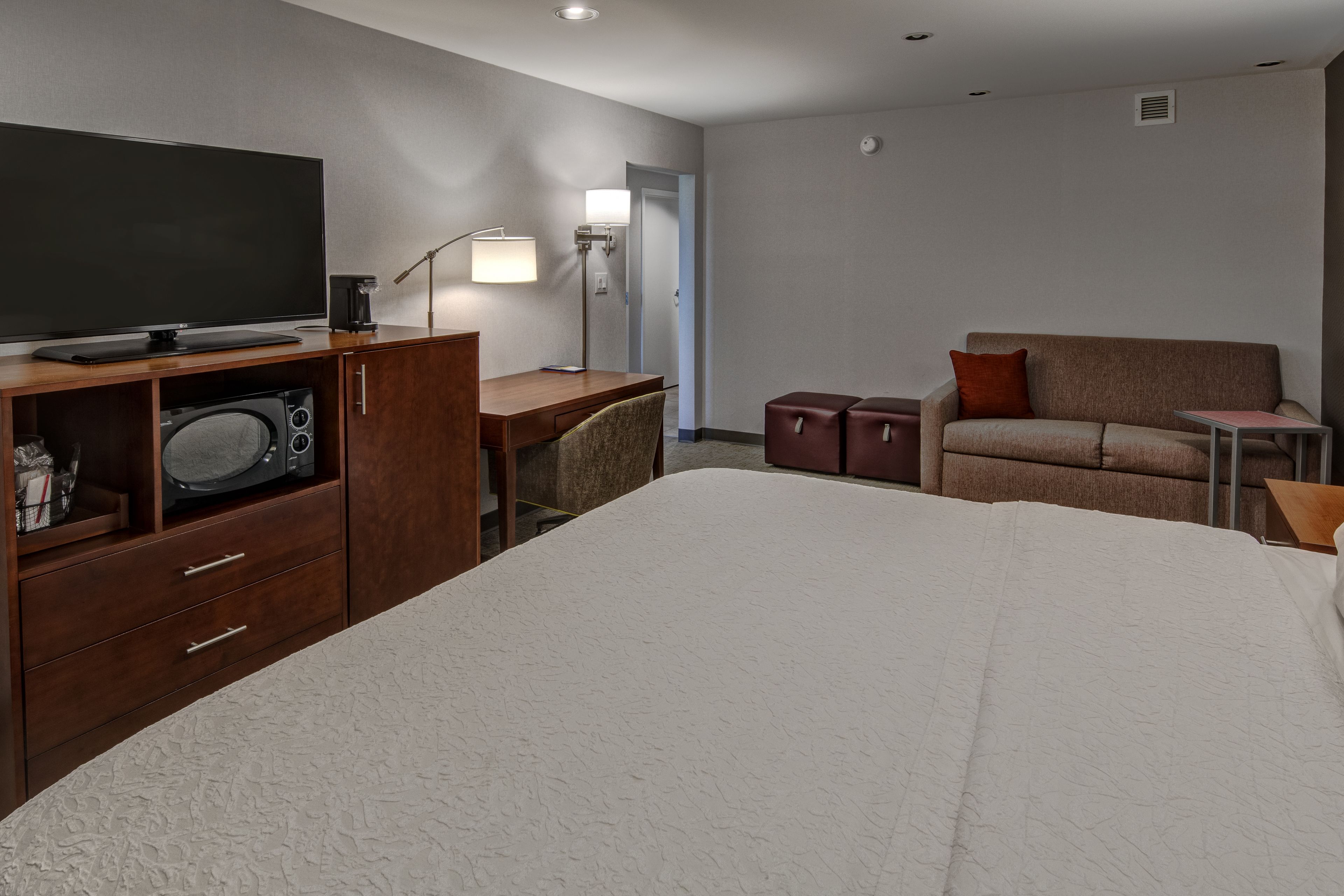 Habitación de hotel con una cama grande, un escritorio con computadora, un televisor de pantalla plana, una cafetera y un sofá.