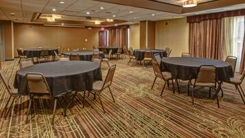 A conference room with multiple round tables and chairs, carpeted flooring, and a large window with curtains.