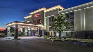 Un hotel moderno con un llamativo letrero de 'Hampton Inn', una entrada cubierta y un estacionamiento.