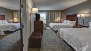 Habitación de hotel con dos camas, televisión, banca y escritorio.