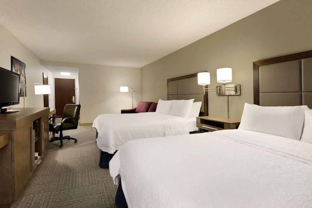 A hotel room with two beds, a desk with a computer, a chair, and a television.