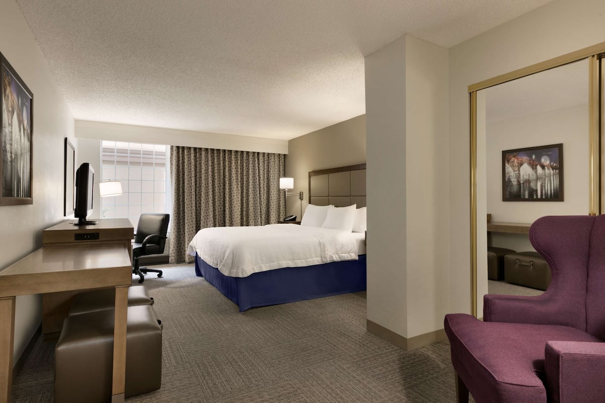 A hotel room with a bed, desk, chair, and a large mirror.