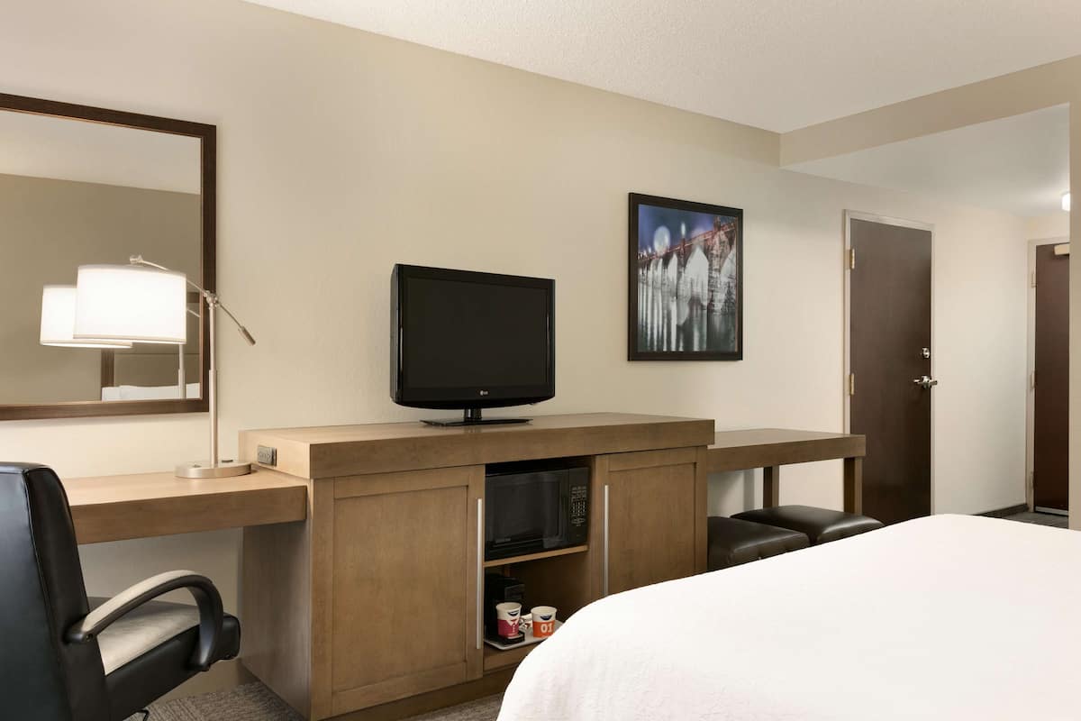 A hotel room with a bed, a desk with a computer, a television, a microwave, and a door.