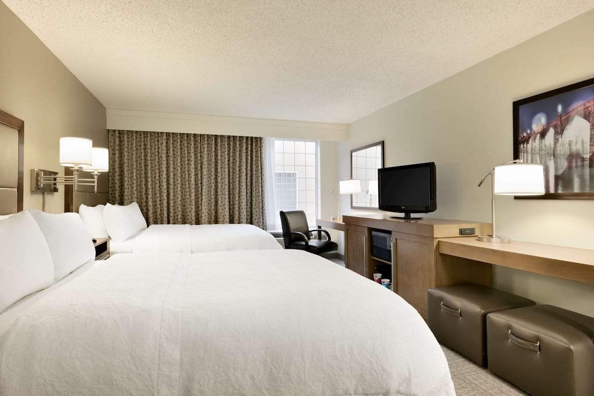 A hotel room with two large beds, a desk with a television, a chair, and a desk lamp.