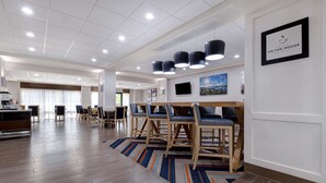 A spacious hotel lobby with a wooden floor, a striped rug, and a dining area with wooden tables and chairs.