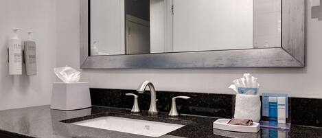 A modern bathroom with a large mirror, a sink with two faucets, and toiletries on the counter.