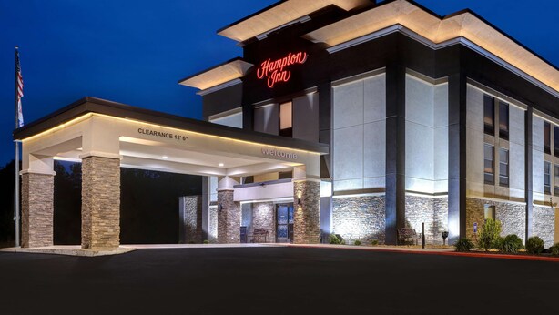 Un hôtel Hampton Inn moderne, avec une entrée bien visible, des piliers en pierre et un panneau lumineux au néon.