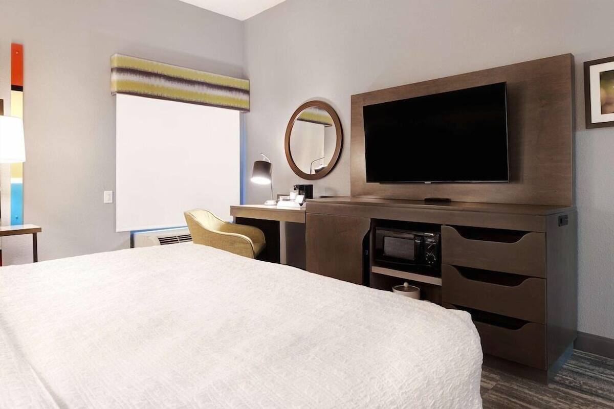 A hotel room with a large bed, a desk with a computer, a flat-screen TV, a microwave, and a minibar.
