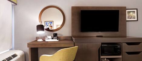 Habitación de hotel con cama, escritorio con computadora, silla, televisor, microondas y espejo.