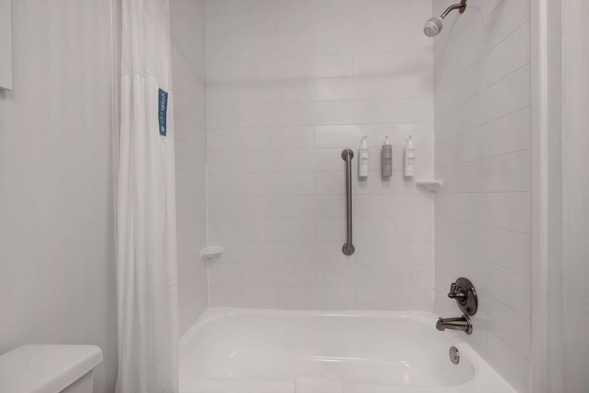 A modern bathroom with a white bathtub, a shower with a handheld showerhead, and a grab bar.