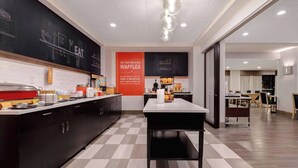 A modern kitchen with a checkered floor, a central table, and a counter with kitchen appliances.
