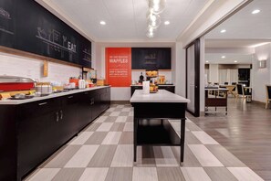 A modern kitchen with a checkered floor, a central table, and a counter with kitchen appliances.