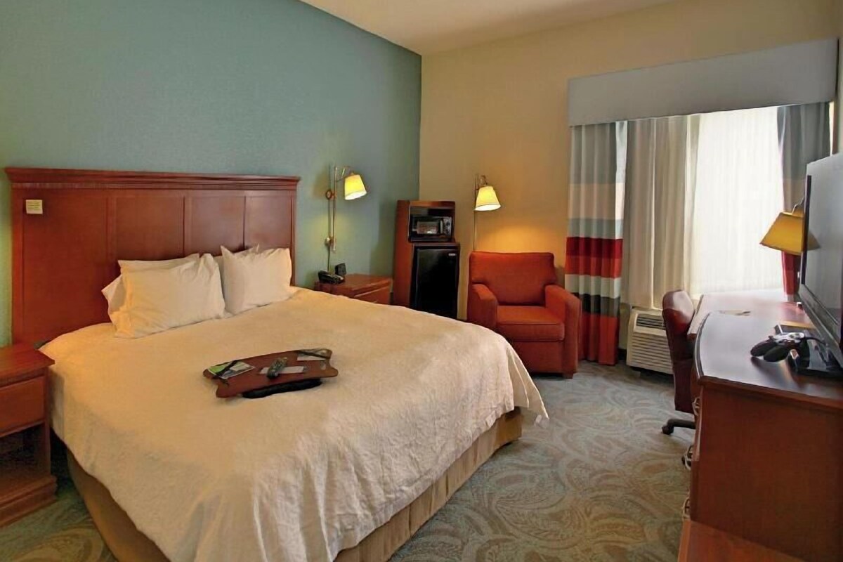A hotel room with a large bed, a desk, a chair, a television, and a microwave.