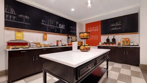 Une cuisine moderne avec des meubles de couleur sombre, un plan de travail en marbre et un mur noir où sont affichés les plats à la carte.